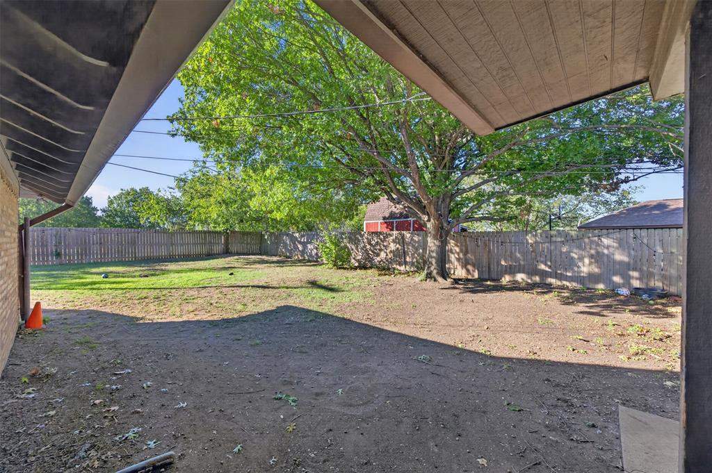 Covered patio area opening to a spacious backyard featuring a wood privacy fence and a mature tree