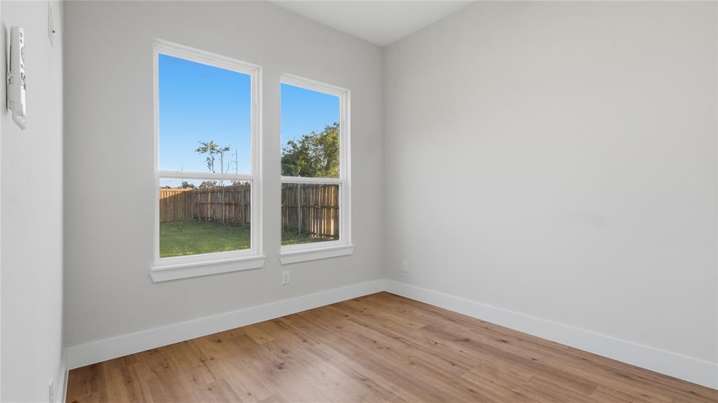 Neutral-toned interior space featuring light wood-finish flooring, dual-pane windows with white trim, and a fenced exterior area