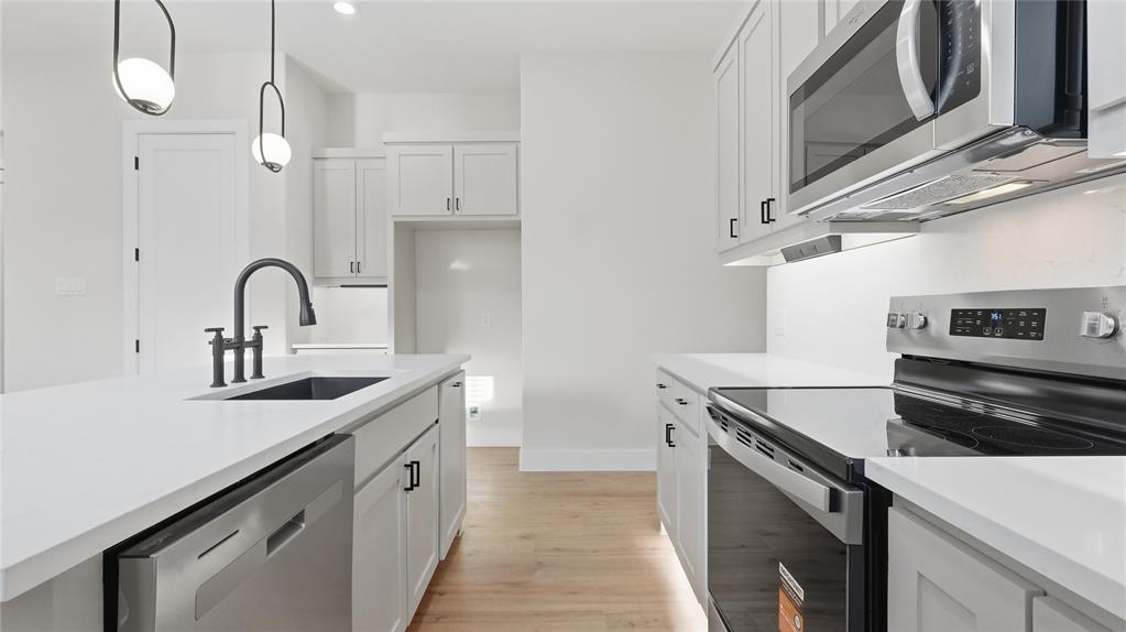 Kitchen featuring shaker-style cabinetry, white countertops, stainless steel appliances, wood-finish flooring, and matte black hardware