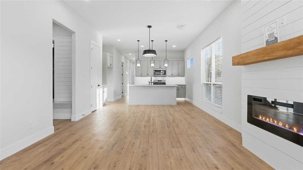 Open floor plan featuring wood-finish flooring, built-in horizontal plank fireplace surround with a natural wood mantel, recessed lighting, and kitchen island with pendant lighting