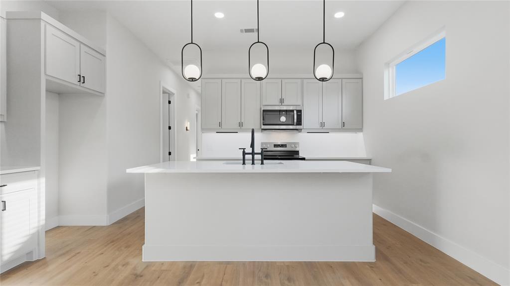 Kitchen featuring a central island with a solid-surface countertop, shaker-style cabinetry, stainless steel appliances, matte black plumbing fixtures, and three glass pendant lights