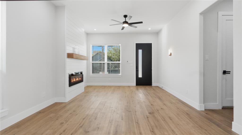 Living area featuring wood-finish flooring, a wall-mounted electric fireplace with a floating wood mantel, horizontal shiplap detailing, a contemporary ceiling fan, and a solid door with a vertical glass pane