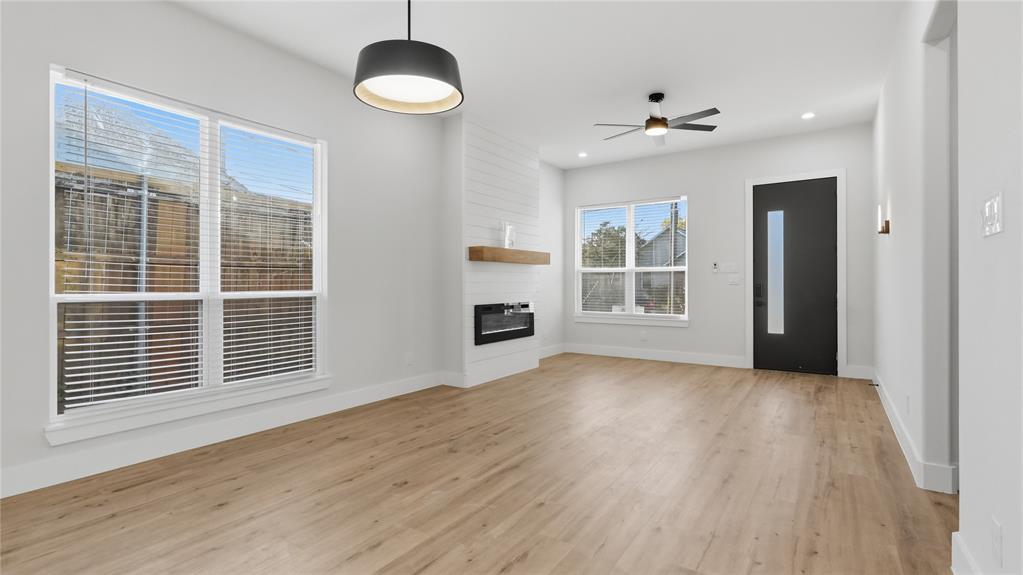 Living area featuring wood-finish flooring, a linear fireplace with a shiplap surround and wood mantel, a contemporary drum pendant light, and a modern entry door with a vertical glass inset