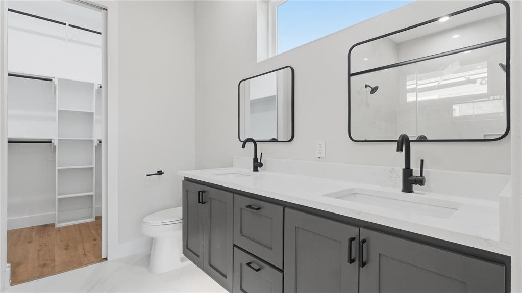 Double vanity featuring dark cabinetry, white countertops with integrated sinks, matte black fixtures, and rectangular mirrors, complemented by a walk-in closet with built-in shelving