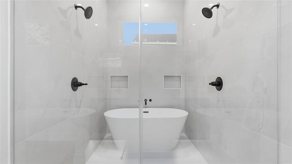 Wet room featuring a freestanding soaking tub, dual wall-mounted showerheads, matte black fixtures, full-height tile surround, and recessed wall niches