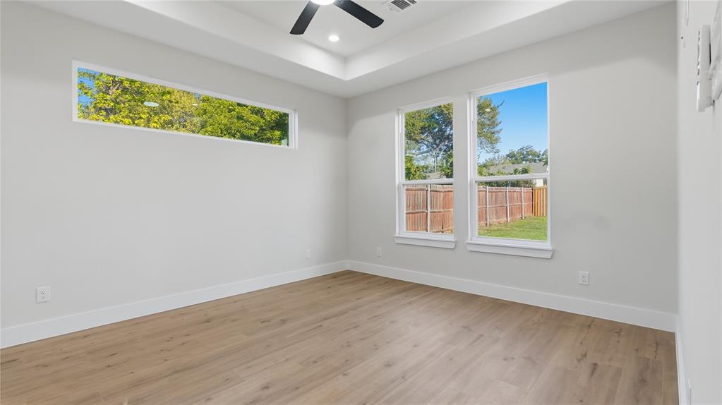 Tray ceiling featuring a central matte black ceiling fan, wood-finish flooring, and expansive windows providing natural light