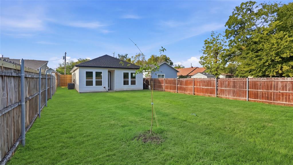 Expansive backyard featuring a large grass lawn, perimeter wood fencing, and a light-toned siding exterior with a dark-finish roof