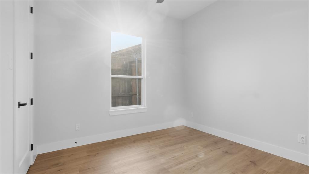 Neutral interior room featuring wood-finish flooring, a single-hung window, and a door with matte black hardware