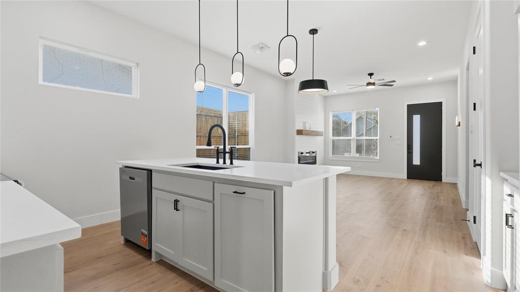 Kitchen island featuring a stone-surface countertop, an integrated sink with a matte black faucet, and pendant lighting