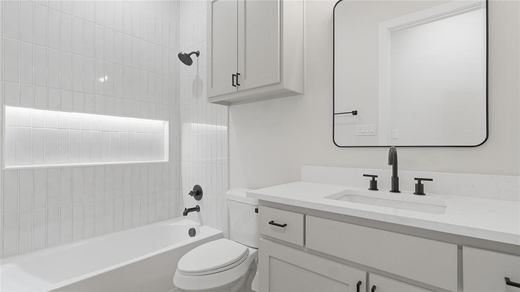 Bathroom featuring a vanity with a white countertop and rectangular undermount sink, matte black hardware, vertical tile surround with built-in recessed shelving, a wall-mounted medicine cabinet, and a rounded rectangular mirror