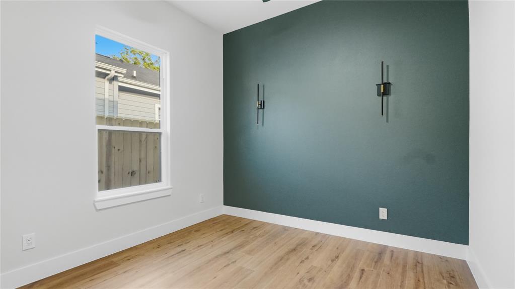 Room featuring wood-finish flooring, a painted accent wall, and two built-in wall-mounted light fixtures