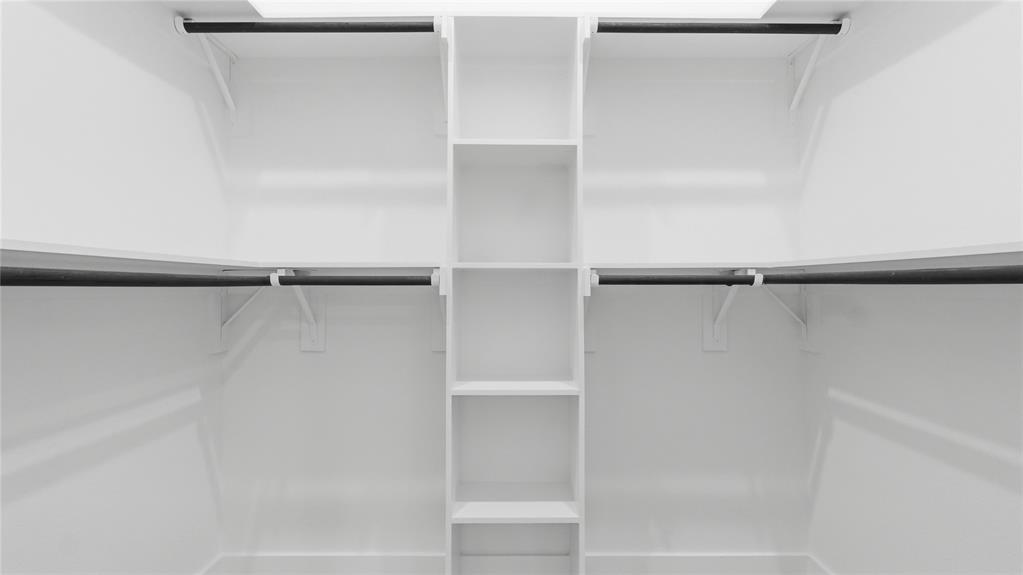 Walk-in closet featuring white built-in shelving, vertical storage tower, and horizontal hanging rods