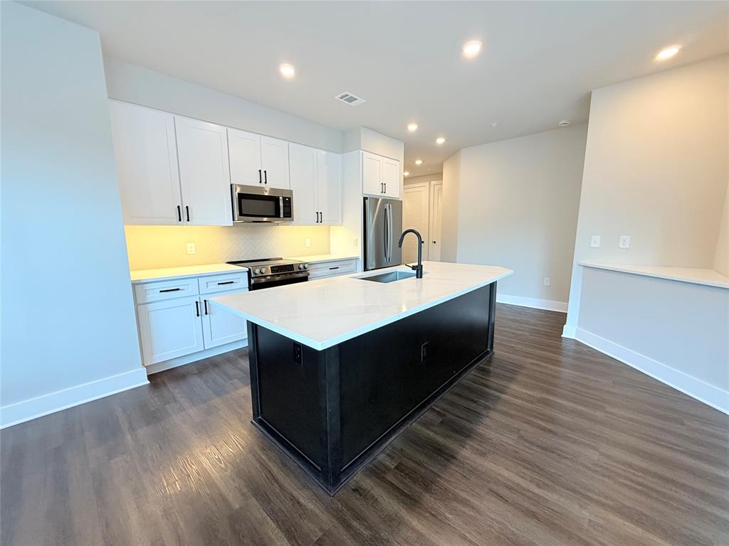 Kitchen with white cabinets, dark cabinets, recessed lighting, a center island with sink, and stainless steel appliances