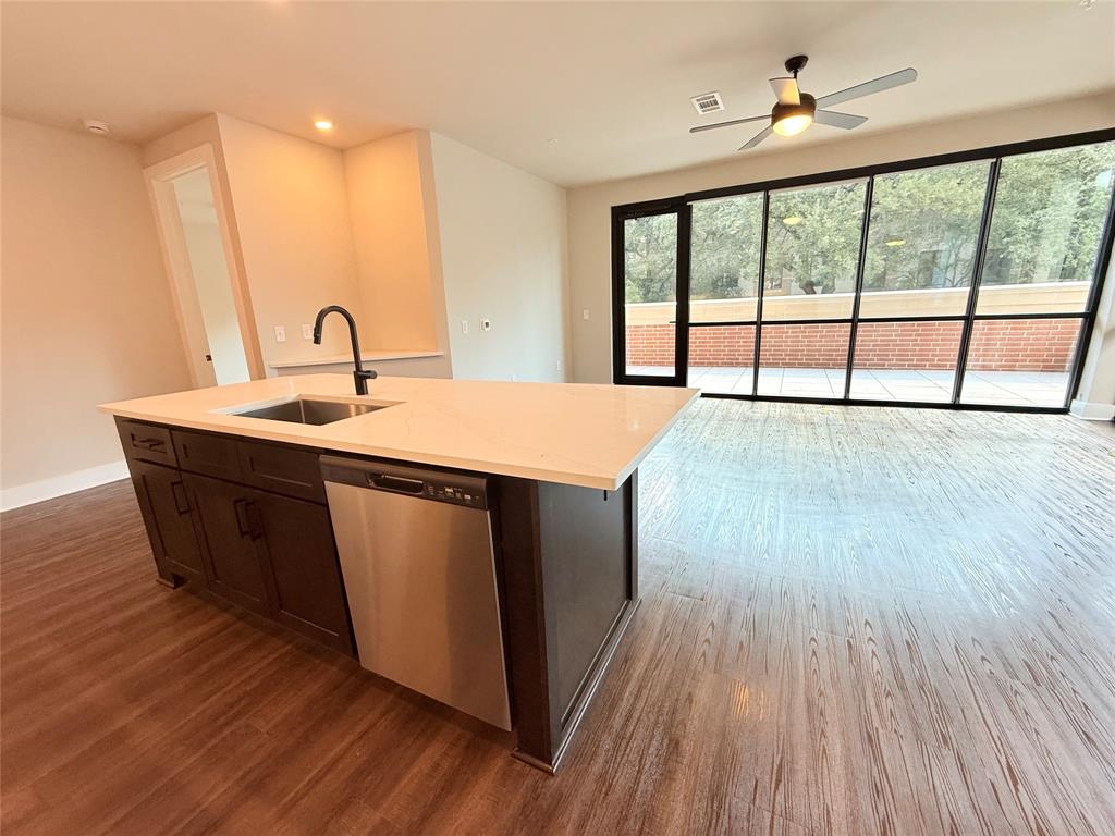 Kitchen featuring stainless steel dishwasher, open floor plan, dark wood-style flooring, dark brown cabinetry, and a kitchen island with sink