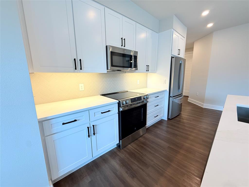 Kitchen with appliances with stainless steel finishes, backsplash, white cabinets, dark wood-type flooring, and recessed lighting
