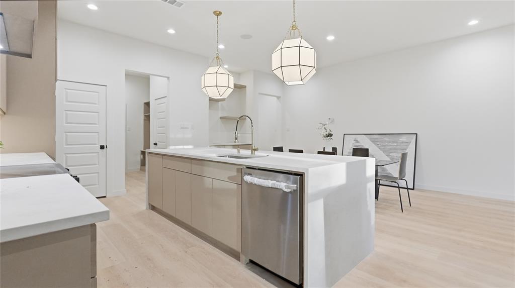 Kitchen featuring a waterfall-edge island with stone-finish countertops, geometric pendant lighting, stainless steel dishwasher, and wood-finish flooring
