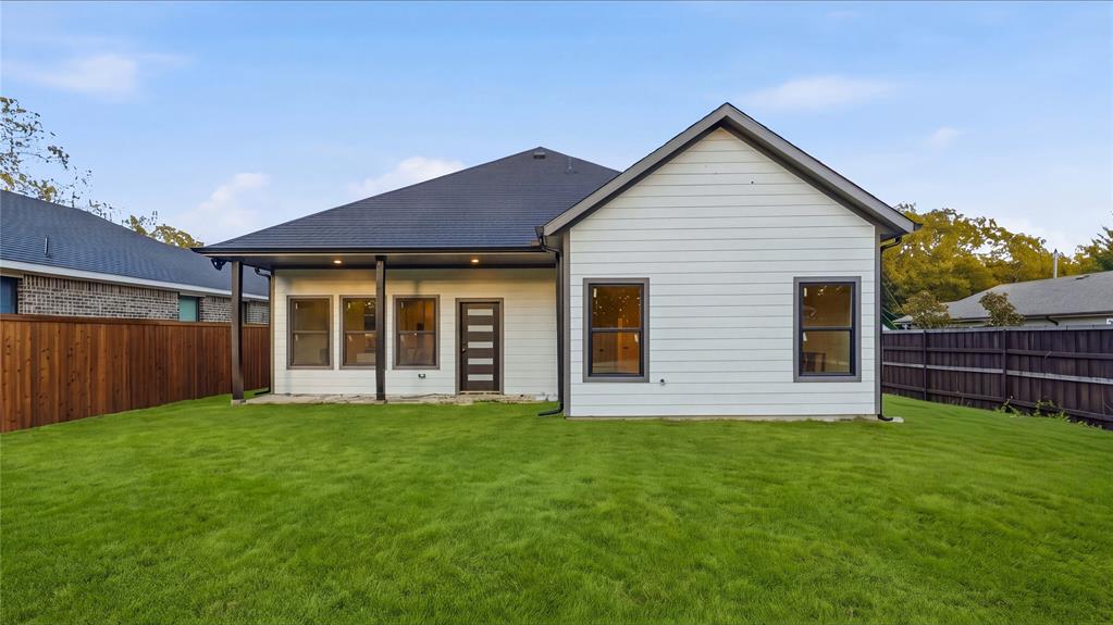 Rear exterior featuring horizontal lap siding, a covered patio with recessed lighting, dark-trimmed windows, a multi-pane glass entry door, and a fenced backyard
