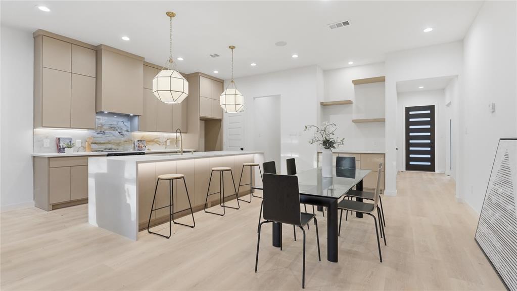 Kitchen featuring flat-panel cabinetry, a quartz waterfall-edge island, geometric pendant lighting, light wood-finish flooring, and a stone slab backsplash