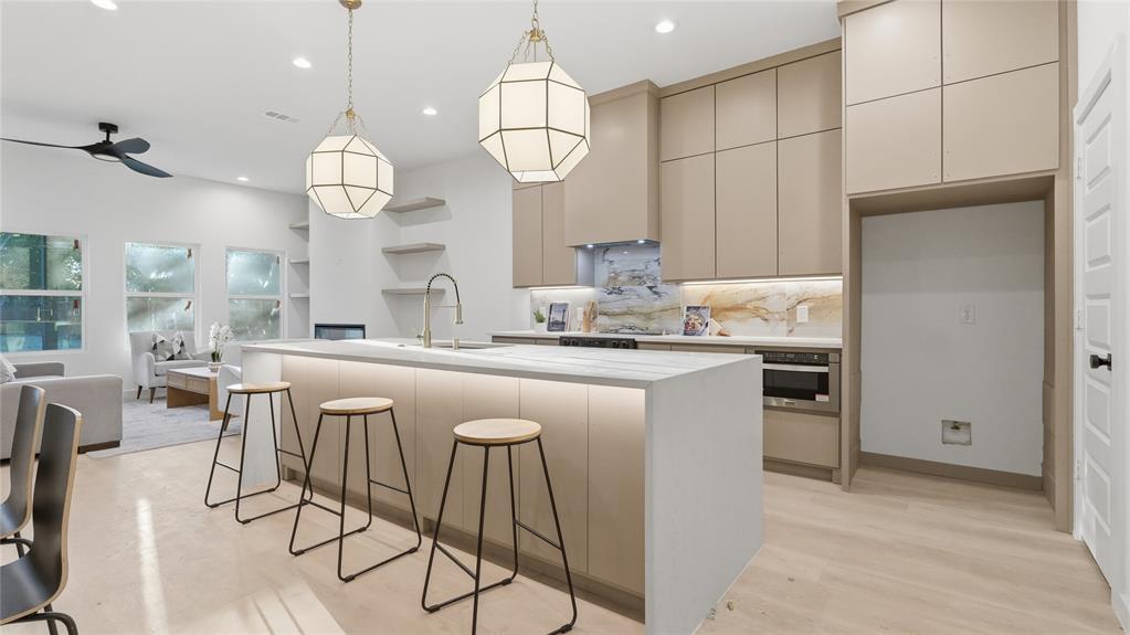 Kitchen featuring floor-to-ceiling cabinetry, a waterfall-edge island with integrated under-cabinet lighting, natural stone backsplash, and recessed pendant lighting