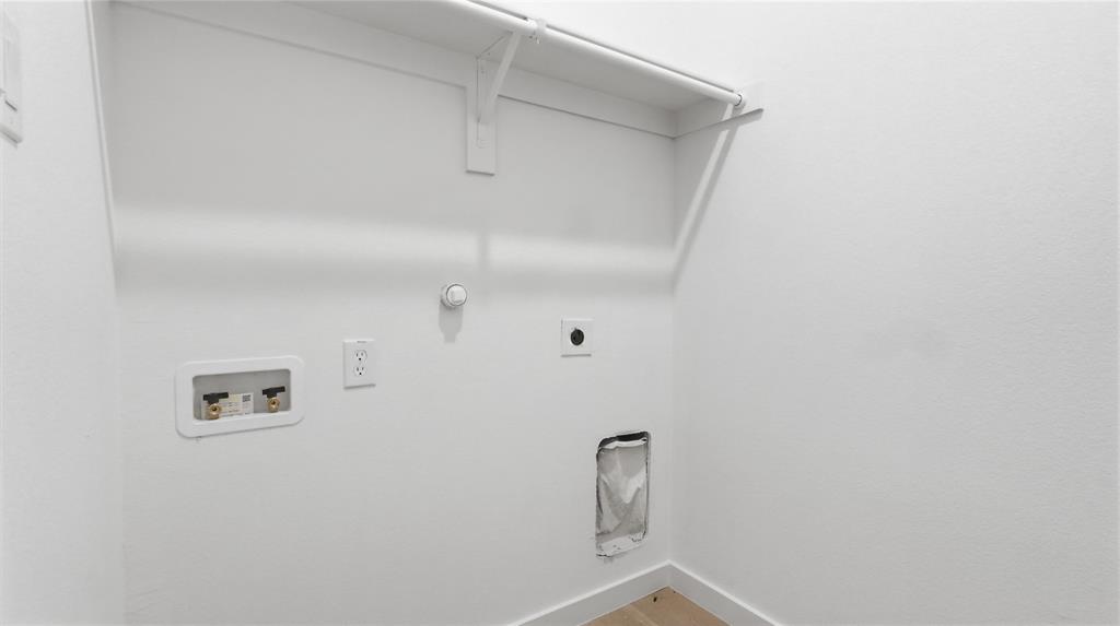 Laundry utility space featuring integrated water hookups, dedicated electrical outlet, and an overhead shelving rod