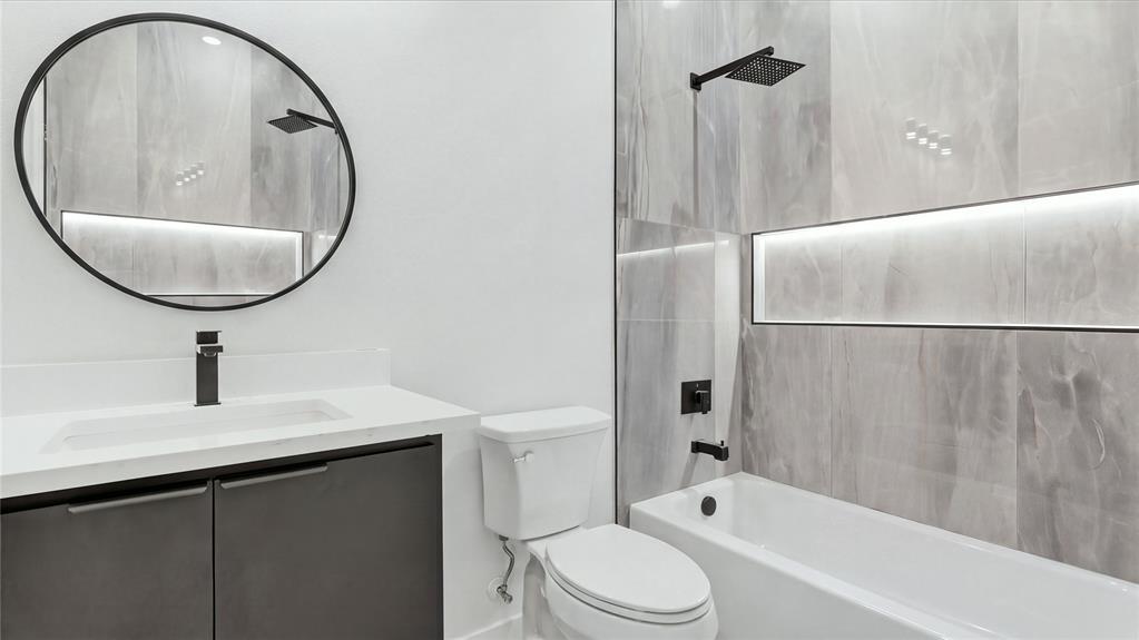 Modern bathroom featuring a dark vanity with a white countertop, circular mirror, matte black fixtures, and large-format wall tile with integrated recessed lighting