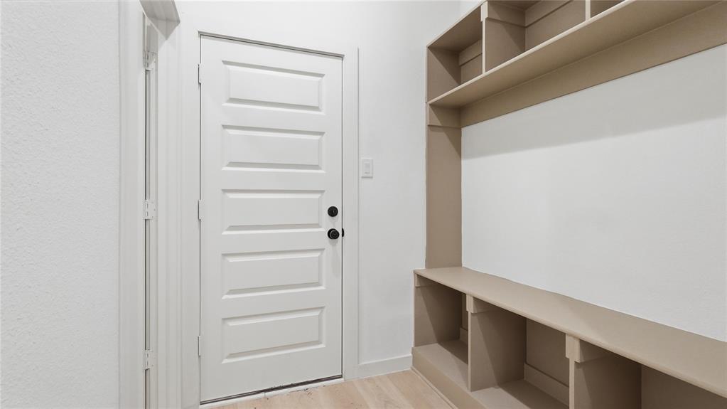 Built-in storage bench featuring open cubbies and overhead shelving, paired with a five-panel interior door and light-toned wood-finish flooring