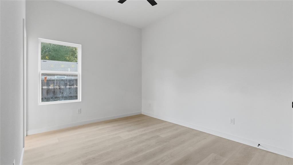 Neutral-toned walls, wood-finish flooring, and a ceiling-mounted fan, illuminated by a single-pane window