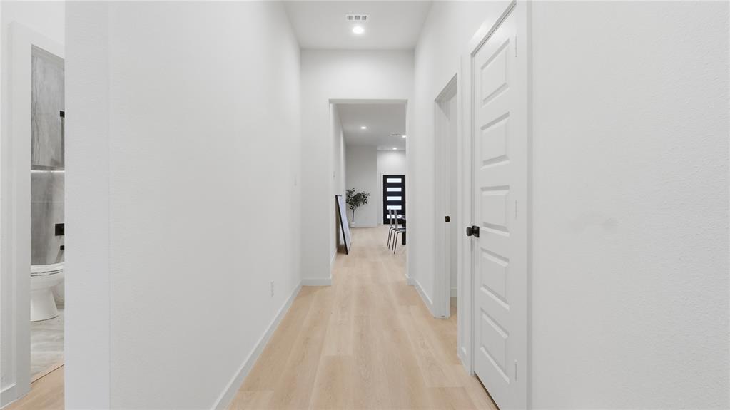 Neutral-toned interior hallway featuring wood-finish flooring, recessed lighting, and five-panel interior doors with matte black hardware