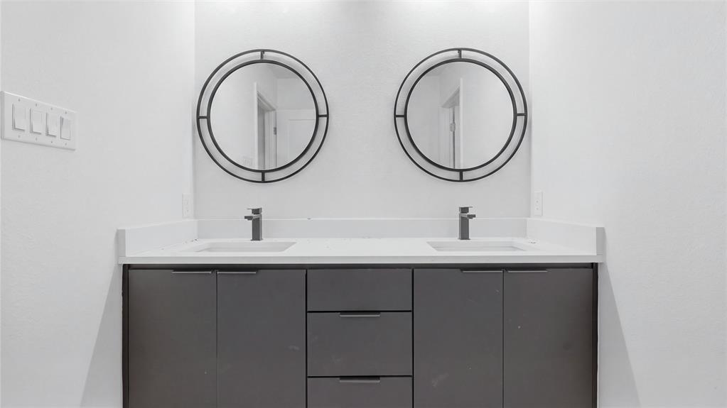 Dual-sink vanity featuring a solid surface countertop, charcoal-toned cabinetry, and two circular mirrors with black frames