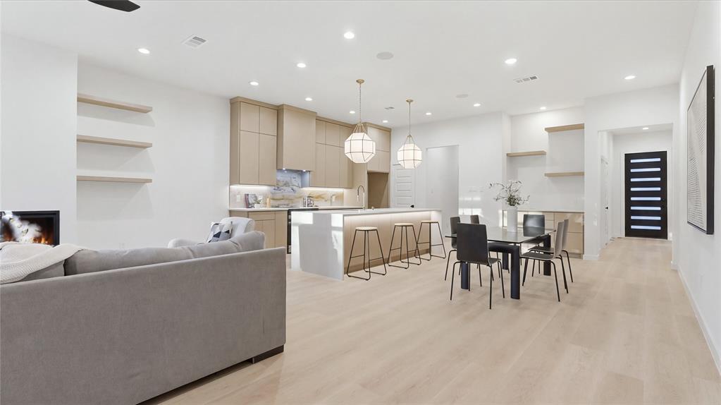 Light-toned wood-finish flooring, custom flat-panel cabinetry, quartz-topped center island with integrated task lighting, recessed ceiling lighting, and built-in floating shelves