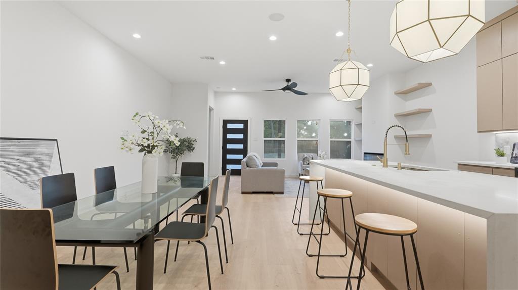 Open-concept space featuring light wood-finish flooring, a waterfall-edge island with integrated under-cabinet lighting, geometric pendant light fixtures, and minimalist built-in wall shelving