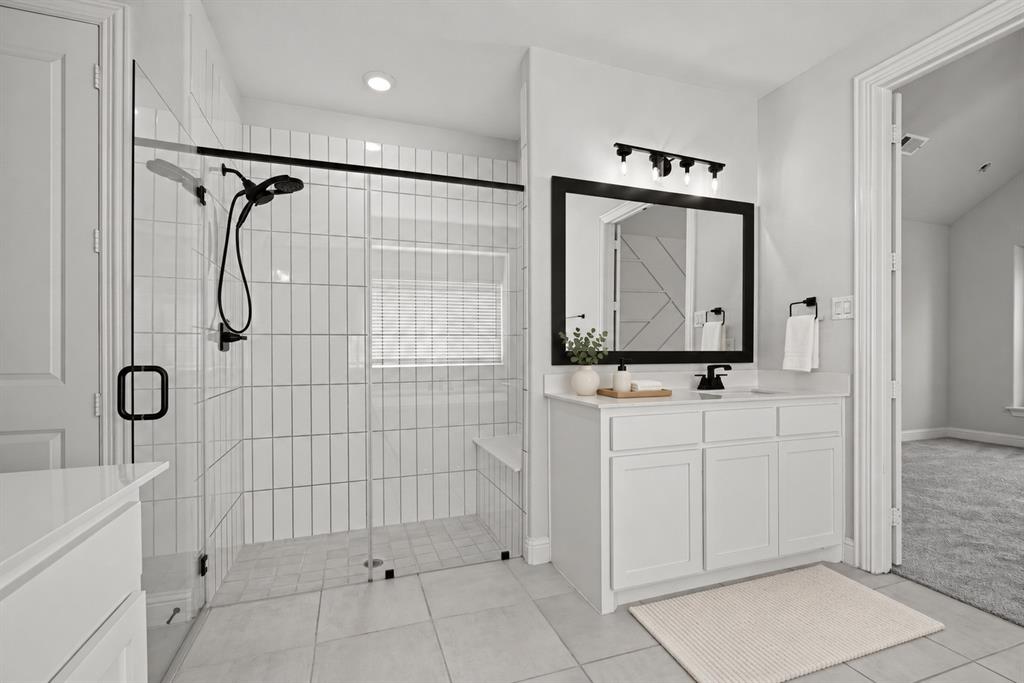Walk-in shower with vertical tile surround, glass enclosure, and matte black fixtures, paired with a white vanity featuring a solid surface countertop and framed mirror