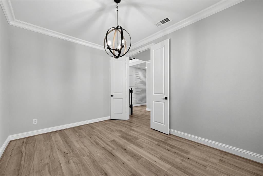 Neutral-toned room featuring wood-finish flooring, crown molding, double doors with matte black hardware, and an orb-style chandelier