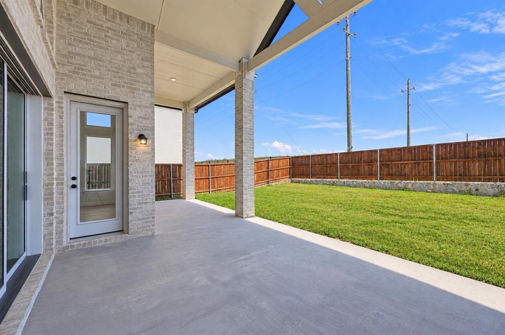 Covered patio with brick-finished pillars, concrete flooring, exterior wall-mounted lighting, wood-style privacy fencing, and stone retaining wall