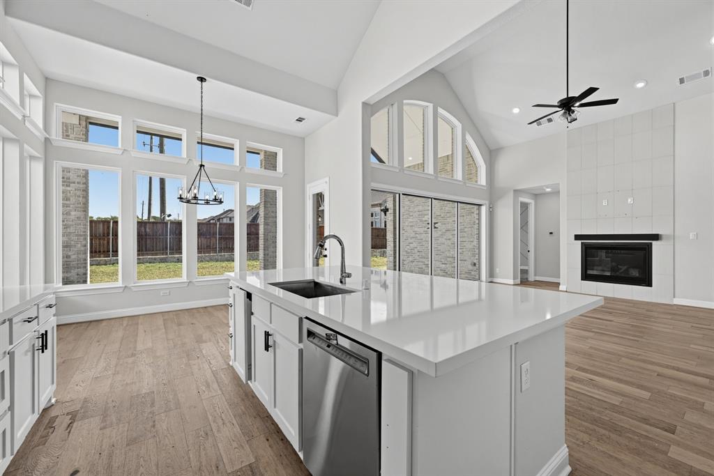 Open-concept interior featuring vaulted ceilings, a central kitchen island with stone countertops, floor-to-ceiling windows, wood-finish flooring, and a fireplace with a floor-to-ceiling tile surround Open-concept interior featuring vaulted ceilings, a central kitchen island with stone countertops, floor-to-ceiling windows, wood-finish flooring, and a fireplace with a floor-to-ceiling tile surround
