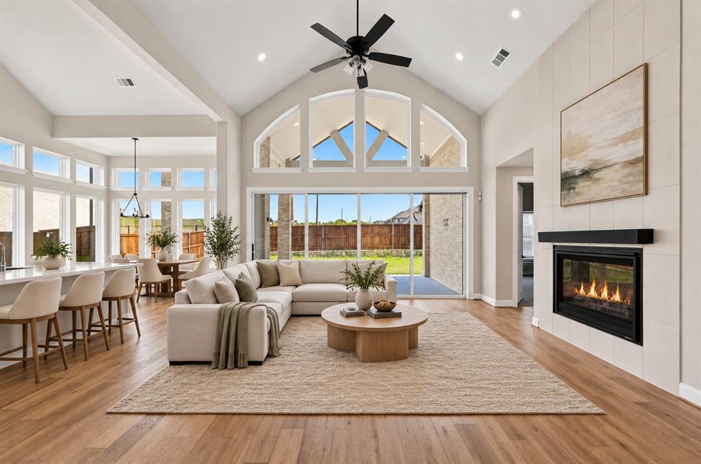 Vaulted ceiling featuring an exposed beam, floor-to-ceiling fireplace with large-format tile surround, expansive multi-pane window wall, and wood-finish flooring Vaulted ceiling featuring an exposed beam, floor-to-ceiling fireplace with large-format tile surround, expansive multi-pane window wall, and wood-finish flooring