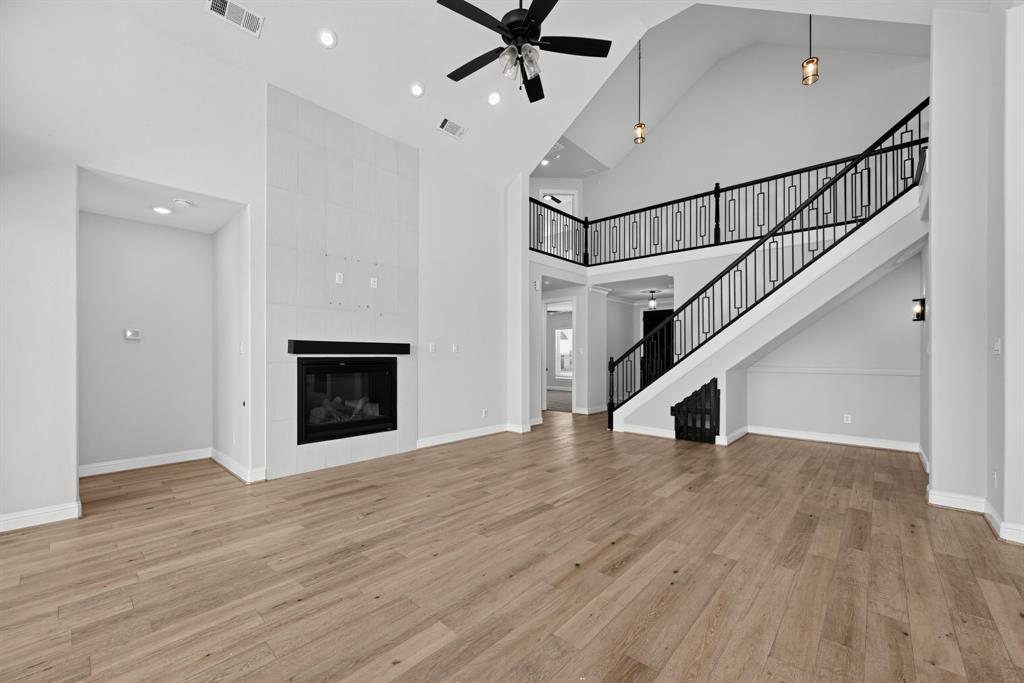 Vaulted ceiling featuring recessed lighting and a central ceiling fan, fireplace with floor-to-ceiling tile surround, and staircase with black metal decorative railing Vaulted ceiling featuring recessed lighting and a central ceiling fan, fireplace with floor-to-ceiling tile surround, and staircase with black metal decorative railing
