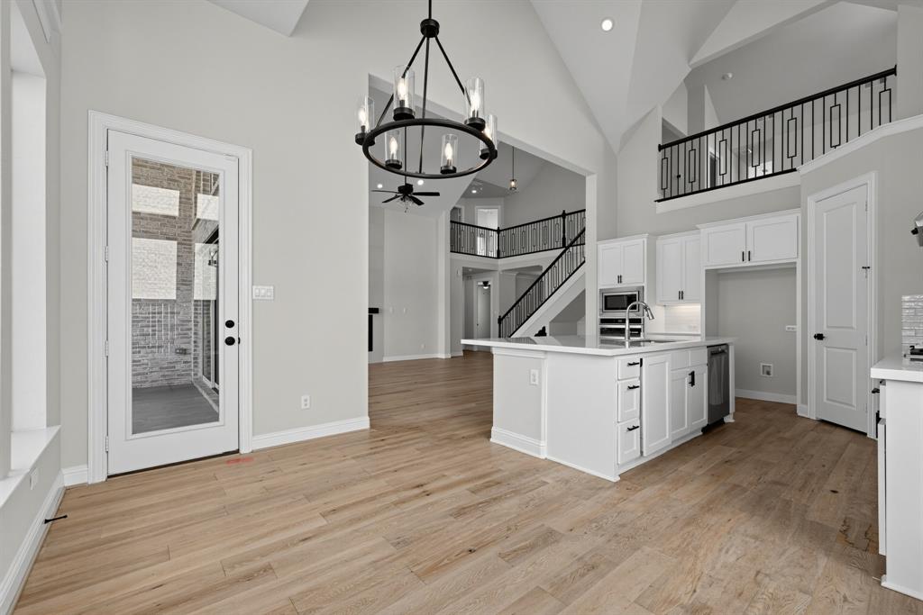 Vaulted ceilings, wood-finish flooring, kitchen island with stone countertop, matte black chandelier, and decorative metal stair railings