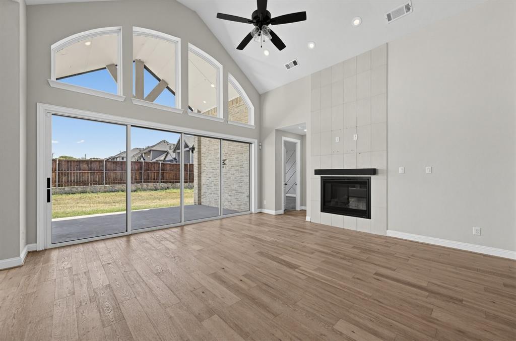 Vaulted ceiling featuring a central black ceiling fan, wood-finish flooring, floor-to-ceiling multi-panel sliding glass doors, and a tiled fireplace surround Vaulted ceiling featuring a central black ceiling fan, wood-finish flooring, floor-to-ceiling multi-panel sliding glass doors, and a tiled fireplace surround