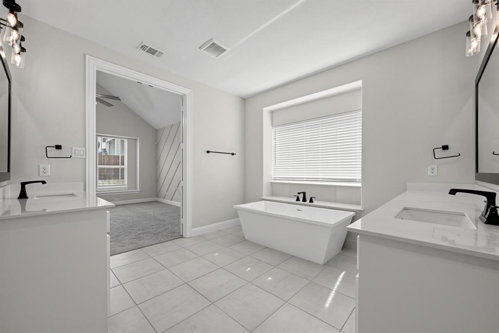 Bathroom featuring dual white vanities with rectangular undermount sinks and light-toned countertops, a freestanding soaking tub, matte black fixtures, and large-format tile flooring