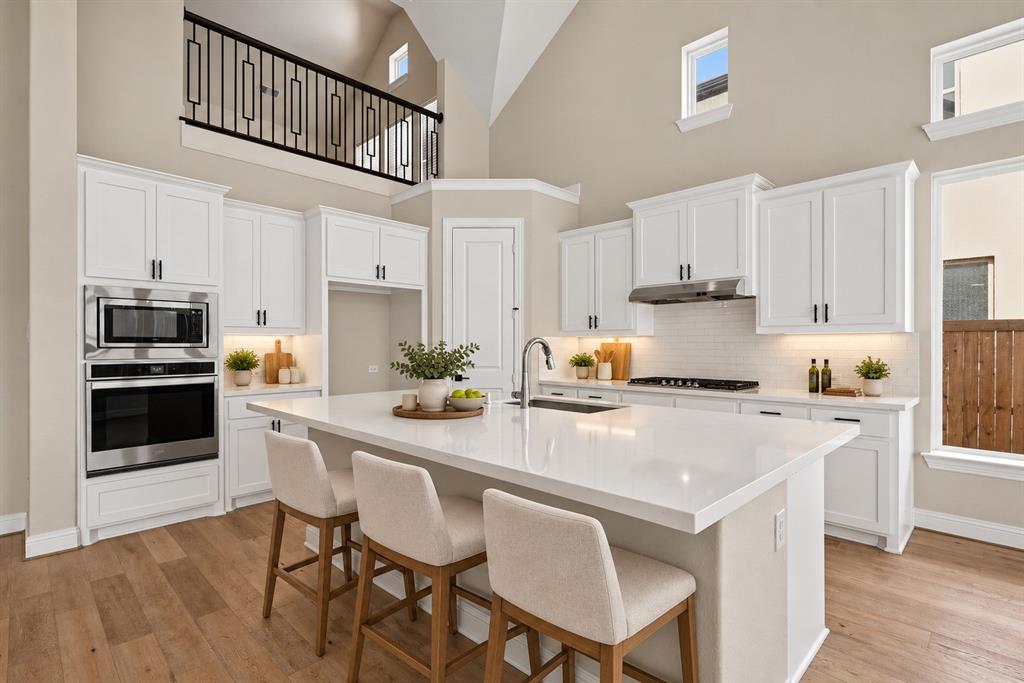 Kitchen featuring white cabinetry, an expansive central island with a solid surface countertop, stainless steel built-in double ovens, vaulted ceilings, and wood-finish flooring