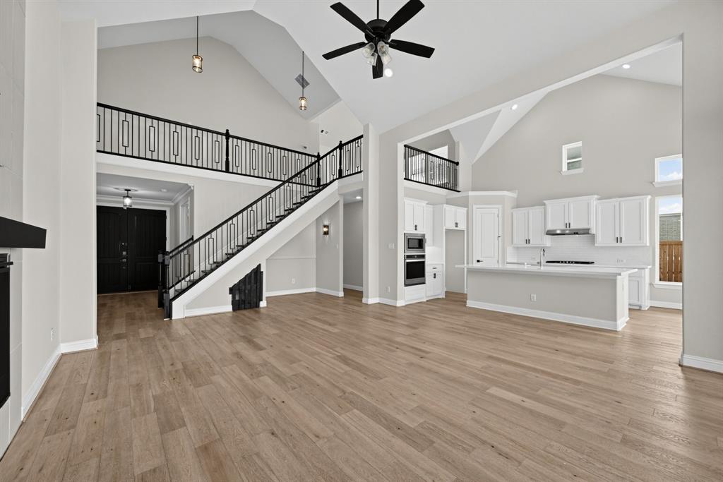 Vaulted ceilings, wood-finish flooring, white cabinetry, a center kitchen island, and a staircase with a black metal railing Vaulted ceilings, wood-finish flooring, white cabinetry, a center kitchen island, and a staircase with a black metal railing