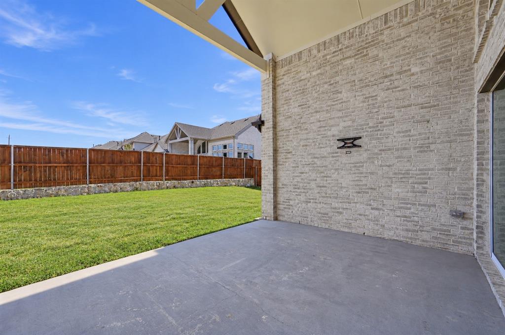 Covered patio featuring a concrete floor, gabled ceiling, brick exterior wall, fenced yard, and stone retaining wall
