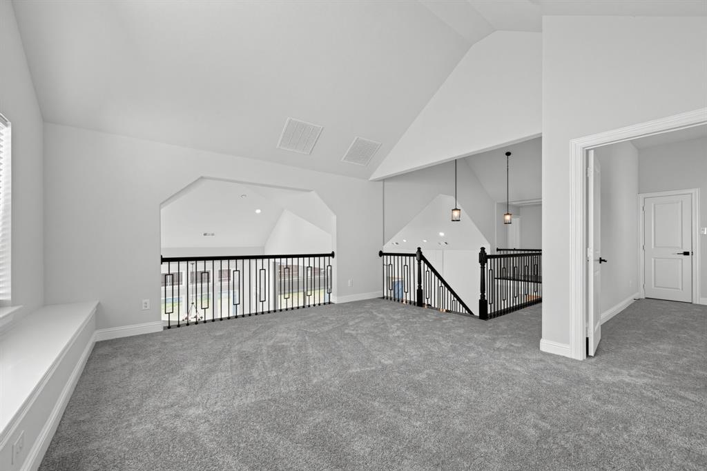 Vaulted ceilings, carpeted flooring, built-in window seating, and decorative black metal balustrade railings with pendant lighting
