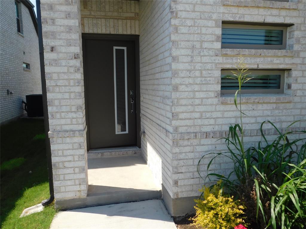 Light-toned brick exterior featuring a recessed entry, modern dark entry door with a vertical glass insert, and stacked rectangular windows