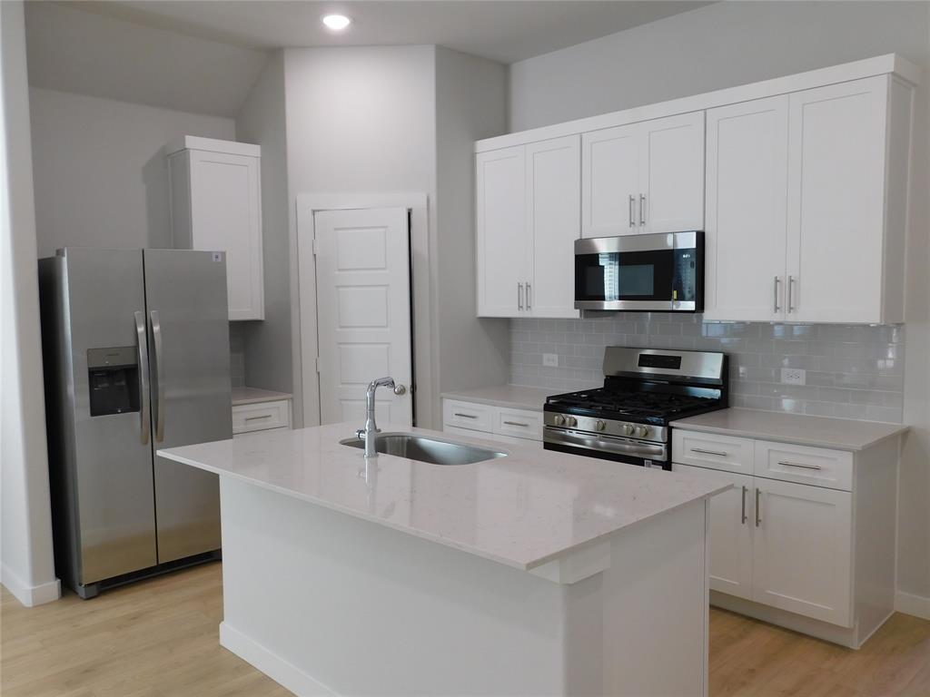 Kitchen featuring white Shaker-style cabinetry, a central island with a stainless steel sink, stone countertops, stainless steel appliances, and subway tile backsplash