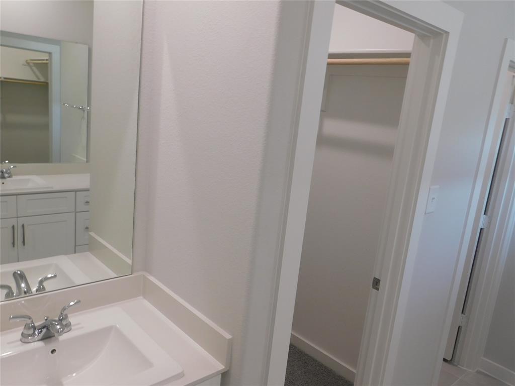 Bathroom featuring a white vanity with a rectangular sink, dual-handle polished chrome faucet, flat-panel cabinetry, and a full-length wall mirror, alongside a walk-in storage area with integrated hanging rods