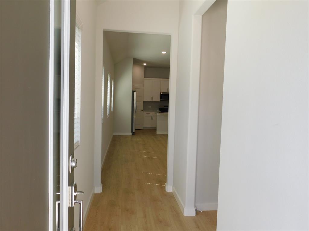 Entryway featuring wood-finish flooring, vaulted ceilings, and recessed lighting, with white cabinetry and stainless steel appliances visible