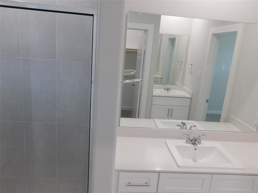 Bathroom featuring a shower with tiled surround, white vanity with countertop sink, and a large wall-mounted mirror