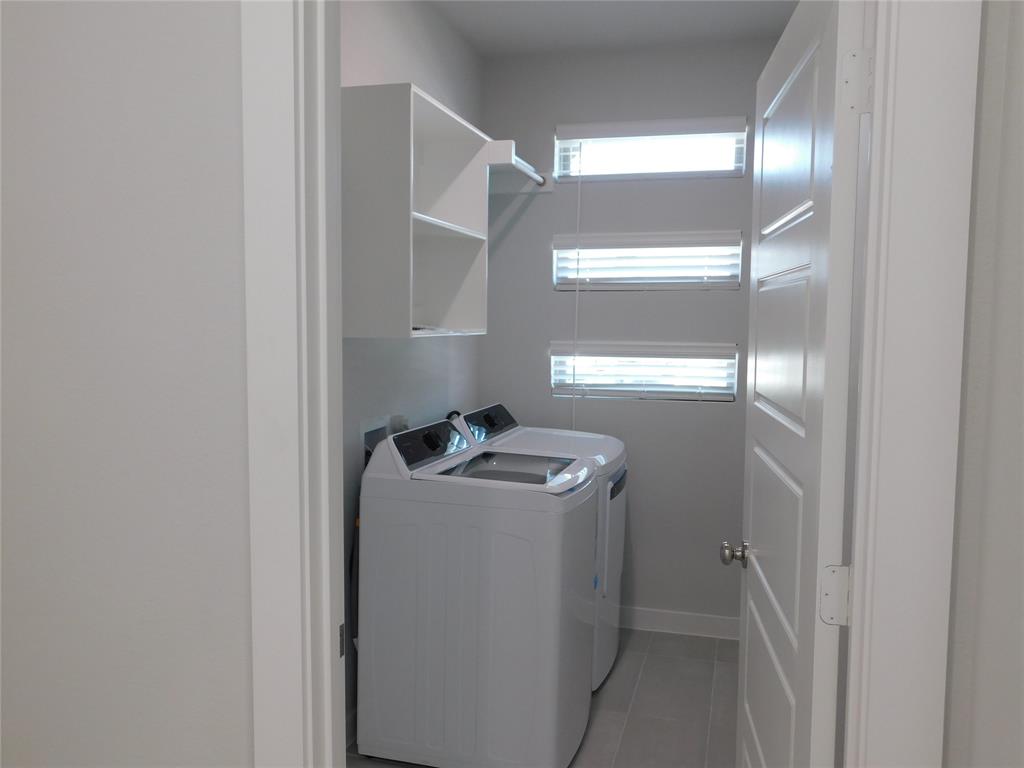 Utility room featuring tile flooring, stacked horizontal windows with blinds, and built-in white shelving with a hanging rod